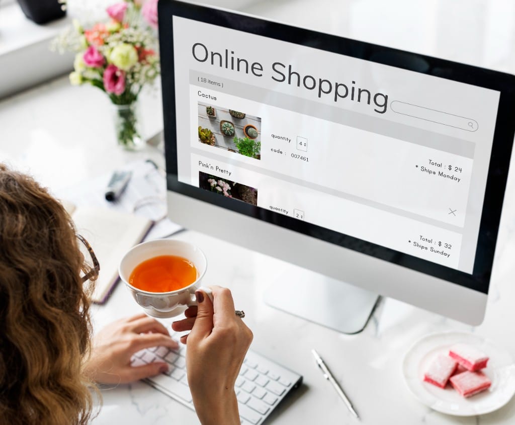 Woman viewing a clean ecommerce shopping cart interface on a desktop computer at a modern marble desk