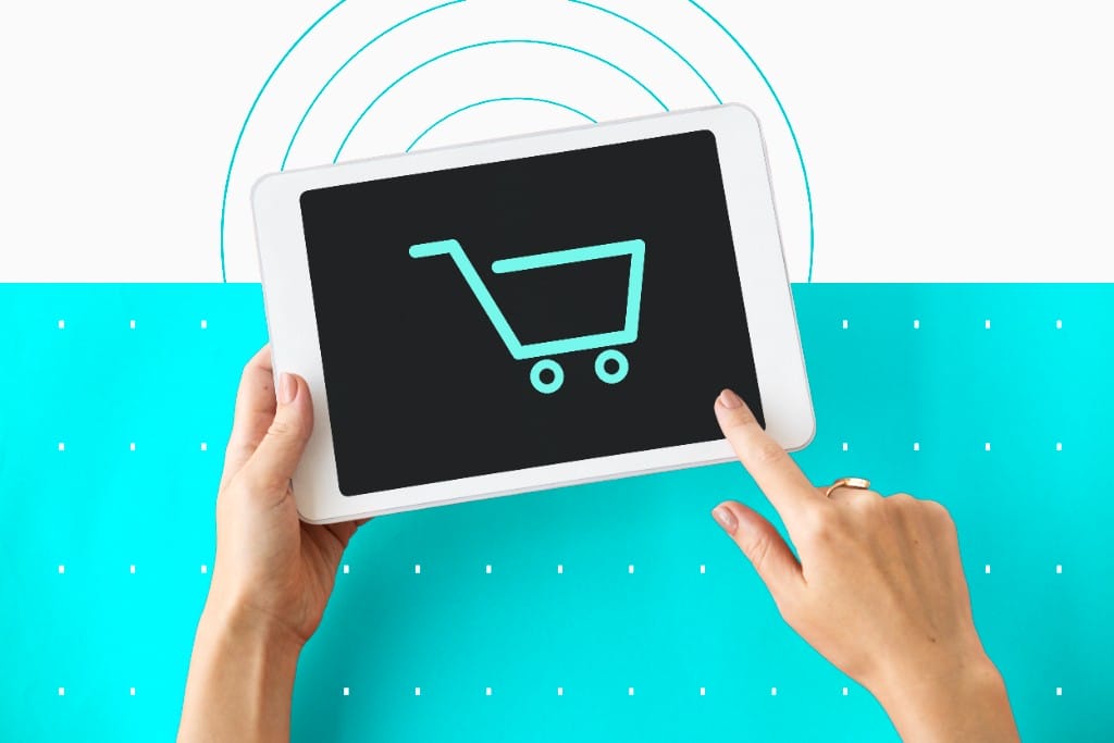 Hands holding a white tablet with a teal shopping cart icon representing ecommerce website design